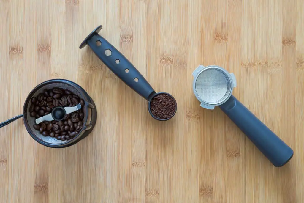 A coffee grinder with beans and scoop with grounds.